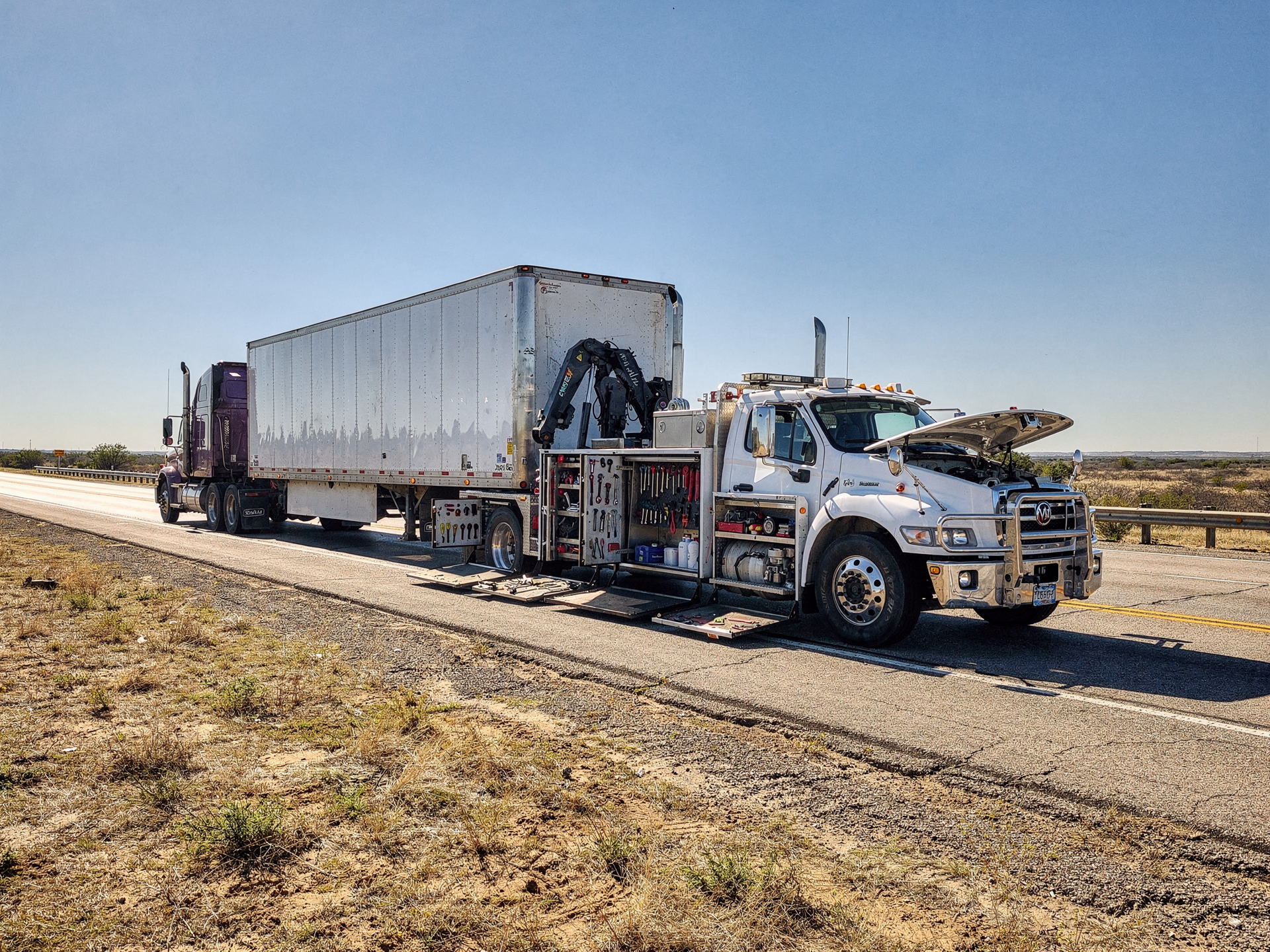 A mobile service rig parked beside a broken-down semi-truck on a sunny Texas highway